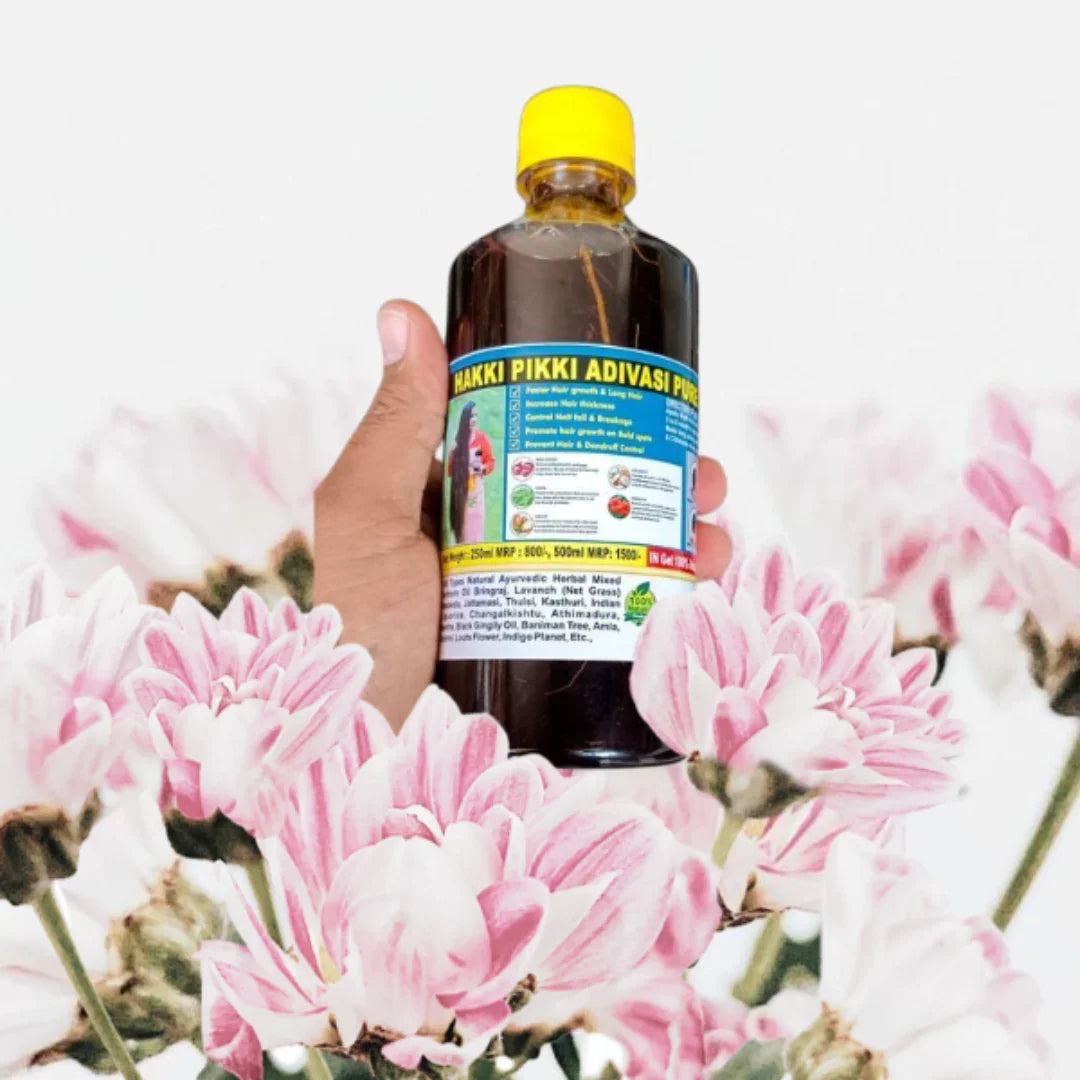 Hakki Pikki Adivasi hair oil for hair growth held above pink flowers with yellow cap bottle