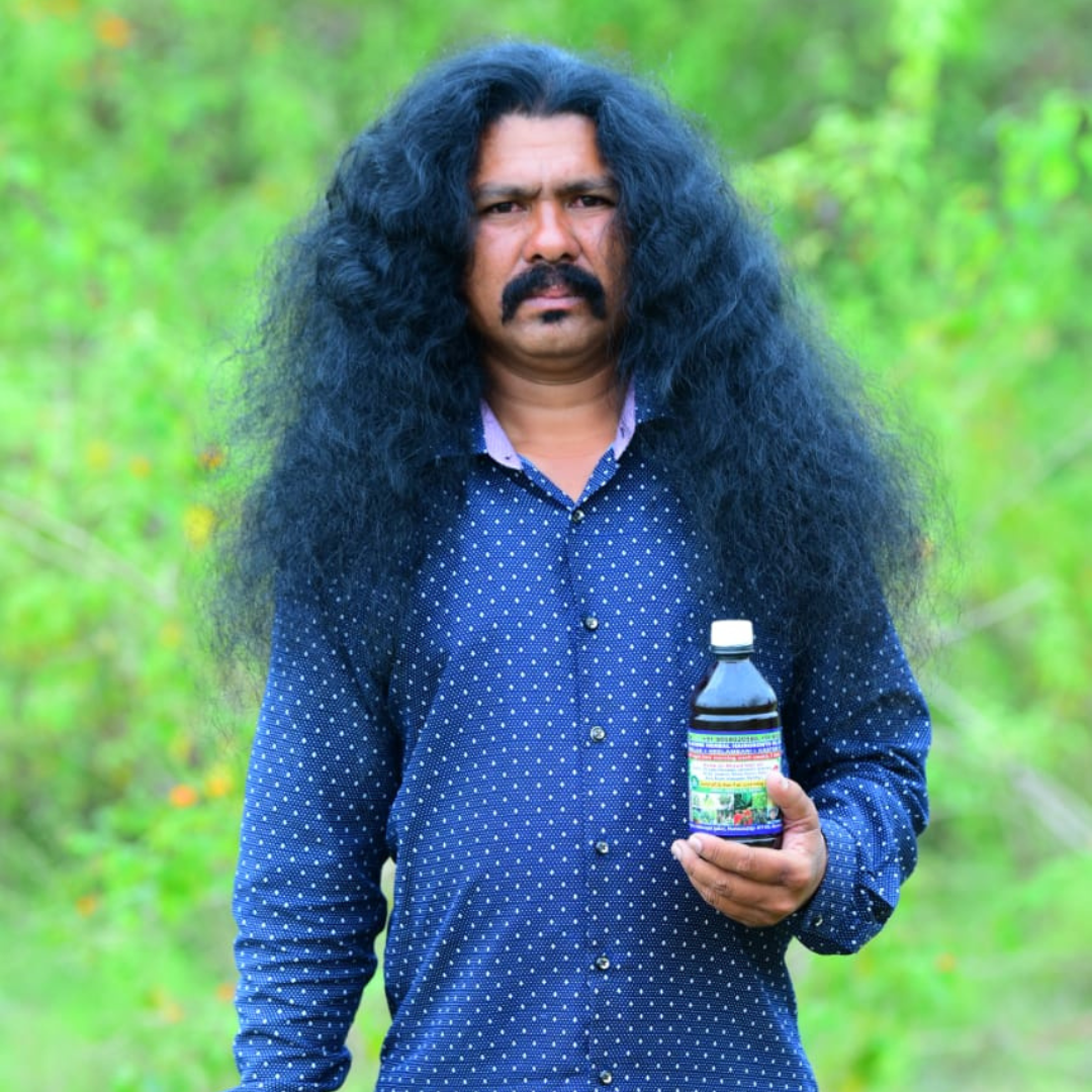Man with long dark hair holding a hakki pikki hair growth oil bottle outdoors